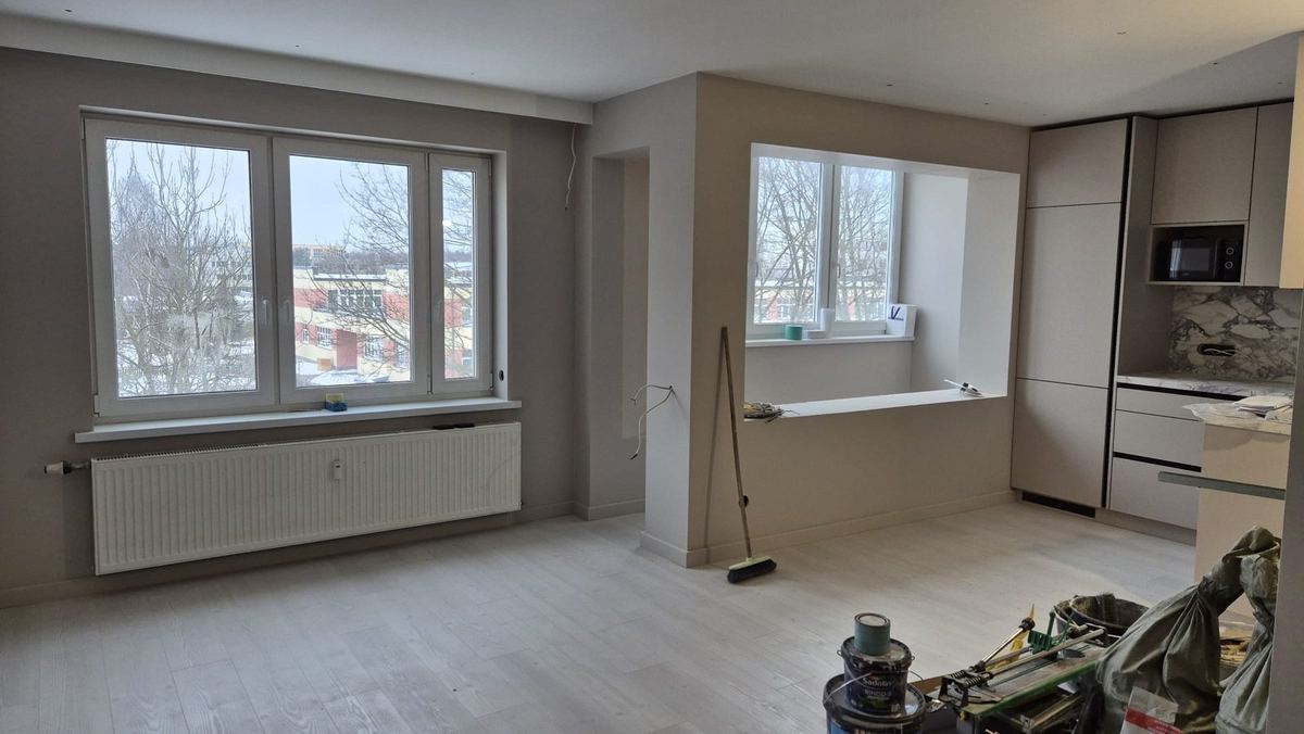 Atjaunota dzīvojamā istaba ar virtuves zonu, gaišu laminātu un iebūvētu nišu pie loga
