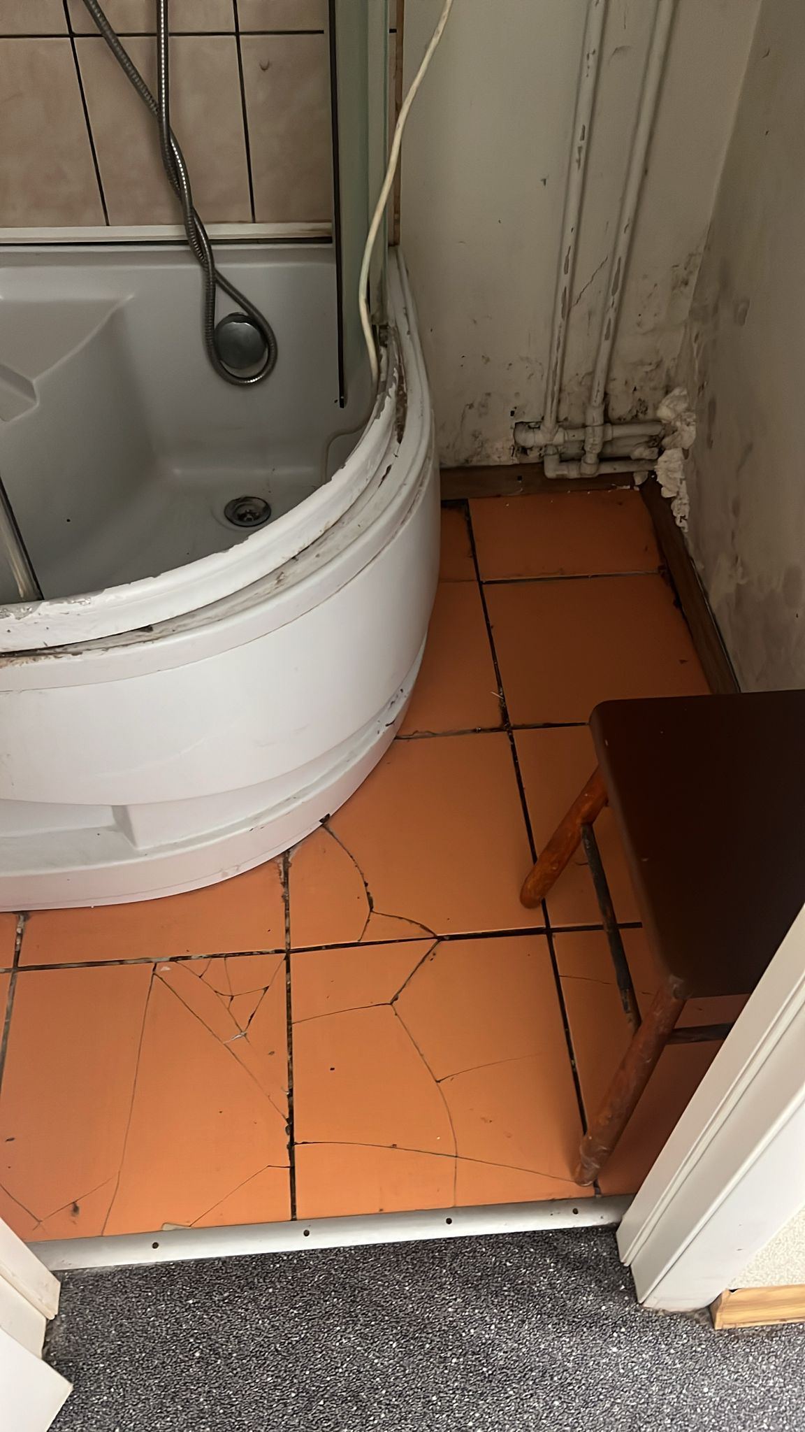 Saplaisājušas grīdas flīzes pie vecās stūra duškabīnes